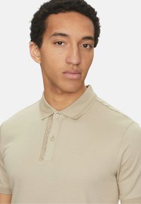 Polo beige realizzato in tessuto liscio, con una patta a bottoni e colletto testurizzato. Logo discreto sul petto.