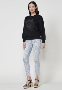 Felpa nera con un motivo animale stilizzato, abbinata a jeans skinny blu chiaro con un motivo leopardo grigio, e sandali con zeppa.