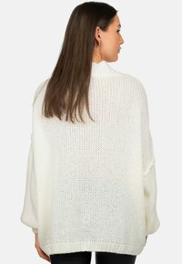 Witte oversized gebreide trui met een losse pasvorm, brede mouwen en ribgebreide manchetten. De textuur is luchtig met een losse steekpatroon.