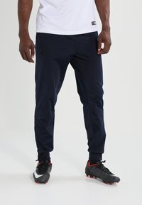 Marine sportleggings met taps toelopend ontwerp, elastische tailleband en zijzakken. Draagt met zwarte voetbalschoenen met rode accenten en witte details.
