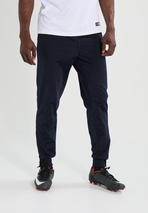 Marine sportleggings met taps toelopend ontwerp, elastische tailleband en zijzakken. Draagt met zwarte voetbalschoenen met rode accenten en witte details.