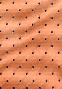 Textil tyg i orange med ribbad yta, med jämnt fördelade svarta prickar. Mönstret är konsekvent över materialet.