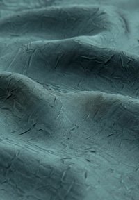 Texturovaná tkanina v hluboké teal barvě, která vykazuje zvrásněný povrch s jemným leskem a nerovnými, organickými vzory po celé ploše materiálu.