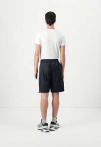 Marine atletiske shorts med elastisk talje og snor, hvide sidelapper og et logo mærke. Bæret med en almindelig hvid t-shirt og sorte sneakers.