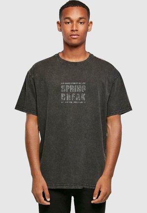 Svart oversized T-skjorte med en falmet print som sier "SPRING BREAK." Har rund hals, korte ermer og en litt slitt tekstur.