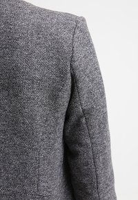 Šedá vlněná bunda s kombinací materiálů a texturovaným vzorem herringbone, s formovanými rameny a čistým, přiléhavým střihem.