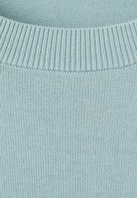 Svetlomodrá pletená látka zobrazujúca rebrovaný golier a hladký textúrovaný diel svetra.