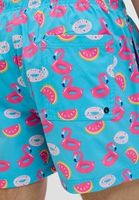 Costumi da bagno di un blu brillante con motivi di fenicotteri rosa, angurie e ciambelle. Presentano una tasca posteriore e una cintura elastica.