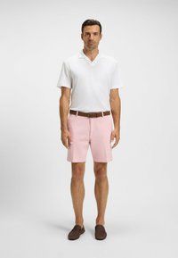White short-sleeve polo shirt, pink shorts with pockets, brown leather belt, and dark brown slip-on shoes, worn by a man.