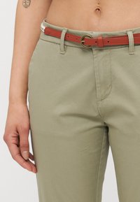 Calças caqui feitas de um tecido macio com uma textura suave, emparelhadas com um cinto castanho que apresenta uma fivela redonda dourada e detalhes de costura visíveis.
