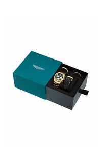 Montre chronographe ton or dans un coffret noir et or avec un bracelet en cuir supplémentaire et deux anneaux métalliques, marque Aston Martin.