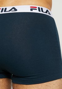 Granatowe bokserki męskie z białą gumką, na której znajduje się napis "FILA" w czarnych i czerwonych literach, gładki materiał i dopasowany krój.