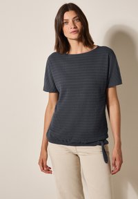 Haut gris foncé à manches courtes avec un motif texturé et rayé, doté d'un détail de ourlet noué. Associé à un pantalon léger à jambe droite.