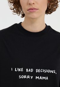 Black cotton t-shirt featuring white printed text: "I LIKE BAD DECISIONS, SORRY MAMA." Crew neck design with a classic fit.