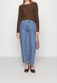 Pull marron à côtes avec des manches longues associé à un jean large taille haute bleu clair. Chaussures à plateforme noires et sac à main en cuir de serpent.