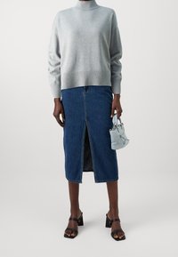 Lichtgrijze trui met geribbelde zoom, gecombineerd met een denim rok tot op de knie met een split aan de voorkant. Zwarte sandalen met blokhak en een kleine blauwe handtas.