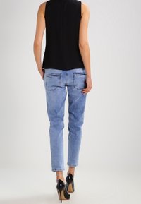Top negro sin mangas, jeans de mezclilla azul claro con bolsillos traseros y tacones altos negros. Textura suave y silueta ajustada.