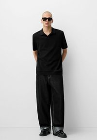 Polo nero con maniche corte, tessuto texturizzato. Abbinato a pantaloni in denim neri larghi e scarpe nere, con orlo a risvolto.