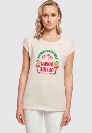 Pink kortærmet t-shirt med et farverigt "Sæsonens Hilsner fra den Upside Down" grafisk design med ferieelementer og "Stranger Things" tekst.