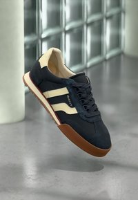 Αθλητικά παπούτσια σε ναυτικό μπλε με κρεμ ρίγες, από σουέντ και συνθετικό υλικό, λάστιχο σόλα με καφέ στοιχεία και στρογγυλή μύτη.