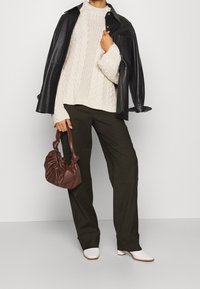 Gruby kremowy sweter w splot warkoczowy, czarna skórzana kurtka, oliwkowe spodnie o szerokich nogawkach, brązowa torebka oraz białe szpilki o ostrym nosku.