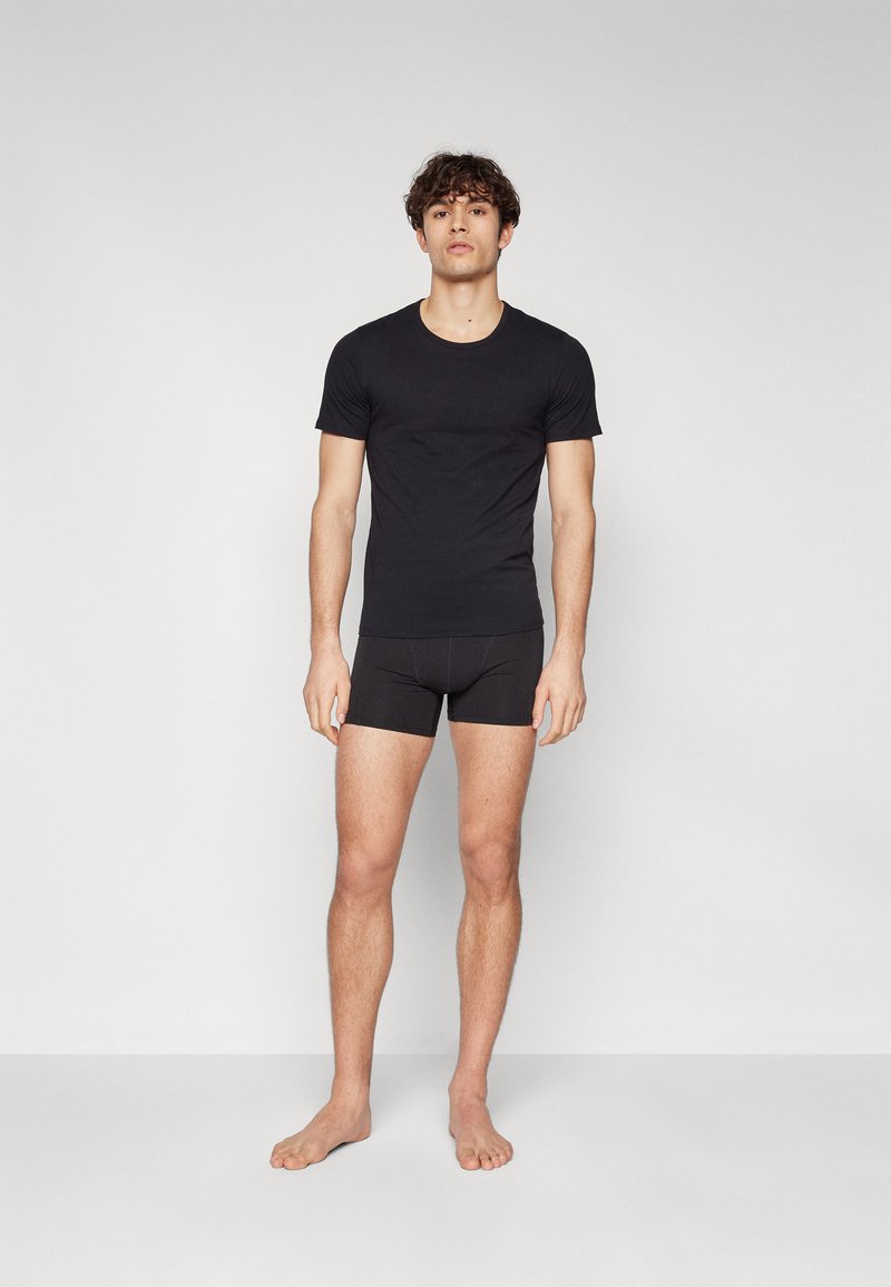 T-shirt noir à manches courtes et boxer assorti, tous deux en tissu lisse, présentant un design ajusté et un minimalisme dans les détails.