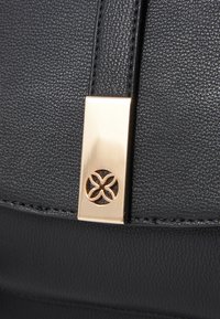 Sac à main en cuir noir avec une surface texturée, du matériel en ton doré et un accent décoratif avec un design découpé floral.