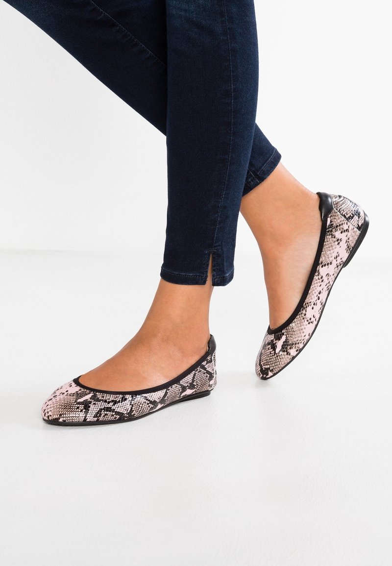 Ballerines avec un design imprimé serpent rose et noir, bout arrondi, bord noir et semelle plate, portées avec un jean foncé.