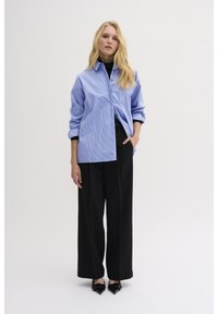 Blue and white striped button-up shirt with a loose fit, paired with black wide-leg trousers and pointed black heels.