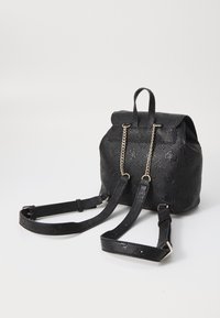 Mochila de cuero negro texturizado con cierre de solapa, detalle de cadena dorada, correas ajustables y patrón floral grabado.