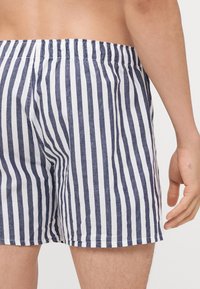 Shorts de bain rayés bleu marine et blanc en tissu léger. Équipés d'une taille élastique et d'une coupe décontractée, ils sont idéaux pour la plage.