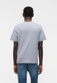 Ανοιχτό γκρι βαμβακερό μπλουζάκι με στρογγυλή λαιμόκοψη, κοντά μανίκια και χαλαρή εφαρμογή, συνδυασμένο με μπλε τζιν παντελόνι που διαθέτει ραφές στην πίσω τσέπη.