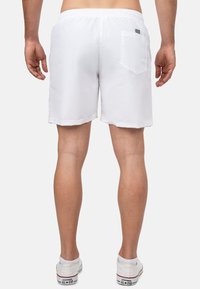 Pantaloni da nuoto bianchi con vita elastica e tasca sul retro. Tessuto morbido e lunghezza fino a metà coscia. Abbinati a sneakers bianche.