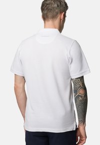 Biała koszulka polo wykonana z bawełny, z klasycznym kołnierzykiem i krótkim rękawem. Subtelne logo na dekolcie, z bocznymi rozcięciami u dołu.