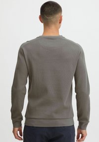 Bawełnowa bluza z okrągłym dekoltem w stonowanym szarym kolorze, z teksturowaną powierzchnią, ściągaczami na rękawach i u dołu. Minimalistyczny design bez widocznych logo.