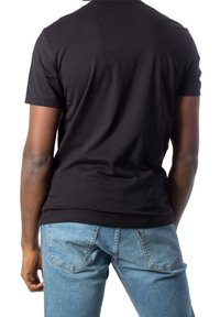 Camiseta de manga corta negra hecha de algodón, diseño ajustado, textura suave, llevada con pantalones vaqueros azul claro que presentan bolsillos traseros y detalles de costura.