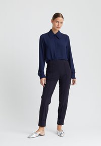 Marineblouse met knoopkraag, lange mouwen en manchetten, gecombineerd met gestructureerde donkere broek en metallic zilveren instappers.