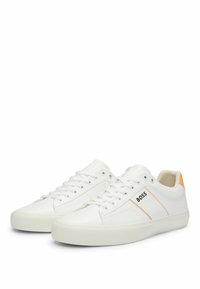 Zapatillas de cuero blancas con acentos naranjas, suela de goma plana, punta redonda y cierre de cordones. Presenta un logotipo negro "BOSS" en el lateral.