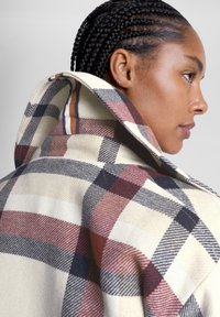 Wool plaid coat featuring large collar, in beige with red, navy, and white checks, displayed with textured fabric and structured silhouette.