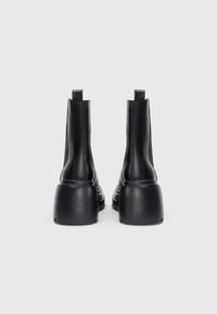 Bottines en cuir noir avec un talon large et haut ; texture lisse, design minimaliste et petites languettes à l'arrière pour un enfilage facile.
