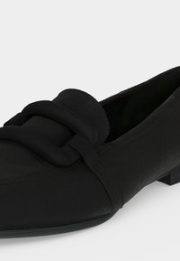 Mocassin en cuir noir avec une grande boucle décorative sur le dessus et un petit talon plat sur fond blanc.