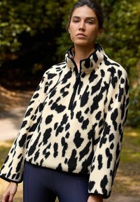 Fleece-tröja med hög krage, med ett abstrakt djurtryck i svart och krämfärgat, dragkedjestängning och avslappnade ärmar.