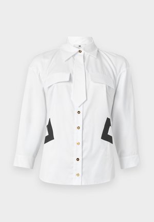 Valkoinen pitkähihainen napillinen paita, jossa on kultaiset napit, kaksi rintataskua, solmionaalto kauluksessa ja mustat geometriset sivukoristeet.