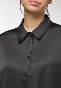 Camicia nera in satin con collo classico, dotata di chiusura con bottoni e una texture liscia e elegante. La leggera lucentezza ne esalta il design.