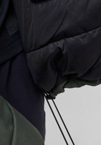 Black puffer jacket with green accents; features textured fabric, elastic cuffs, and adjustable drawstrings on the hem and sleeves.