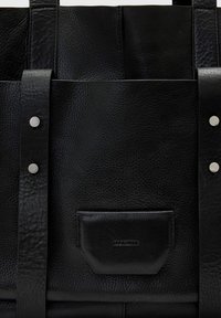 Μαύρη δερμάτινη τσάντα με υφή, ασημένια εξαρτήματα και μπροστινή θήκη με ανάγλυφο λογότυπο. Περιλαμβάνονται ρυθμιζόμενοι δερμάτινοι ιμάντες.