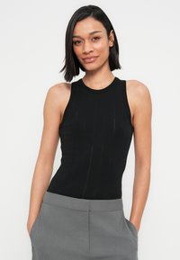 Haut noir sans manches avec une texture côtelée et des rayures verticales subtiles, associé à un pantalon gris avec des poches latérales.