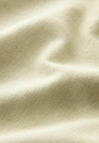 Vaaleanbeige kangas, jossa on sileä pinta, pehmeät poimut ja hienovarainen kudontakuvio. Materiaali näyttää kevyeltä ja hengittävältä.