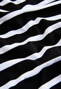 Mustvalge triibuline kangas pehme ja sileda tekstuuriga; triibud on ebakorrapärased, lainelised, mis loob dünaamilise visuaalse efekt.