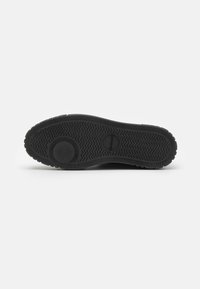 Suela de zapato de goma negra con un patrón de agarre texturizado y detalles circulares, diseñada para ofrecer tracción y estabilidad. Los materiales parecen duraderos y flexibles.